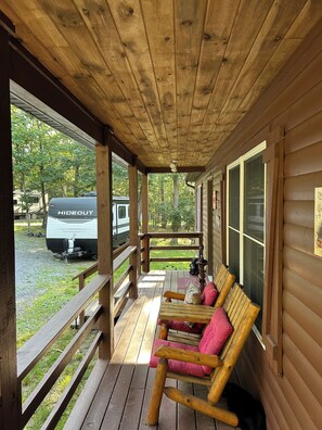 A covered porch with wooden benches and a view of a campsite.