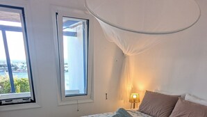 Une chambre à coucher avec un lit, deux fenêtres, une lampe et une vue sur la mer.