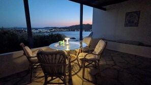 Un patio al aire libre con una mesa redonda y cuatro sillas, con vista a un paisaje costero con edificios y colinas en la distancia.