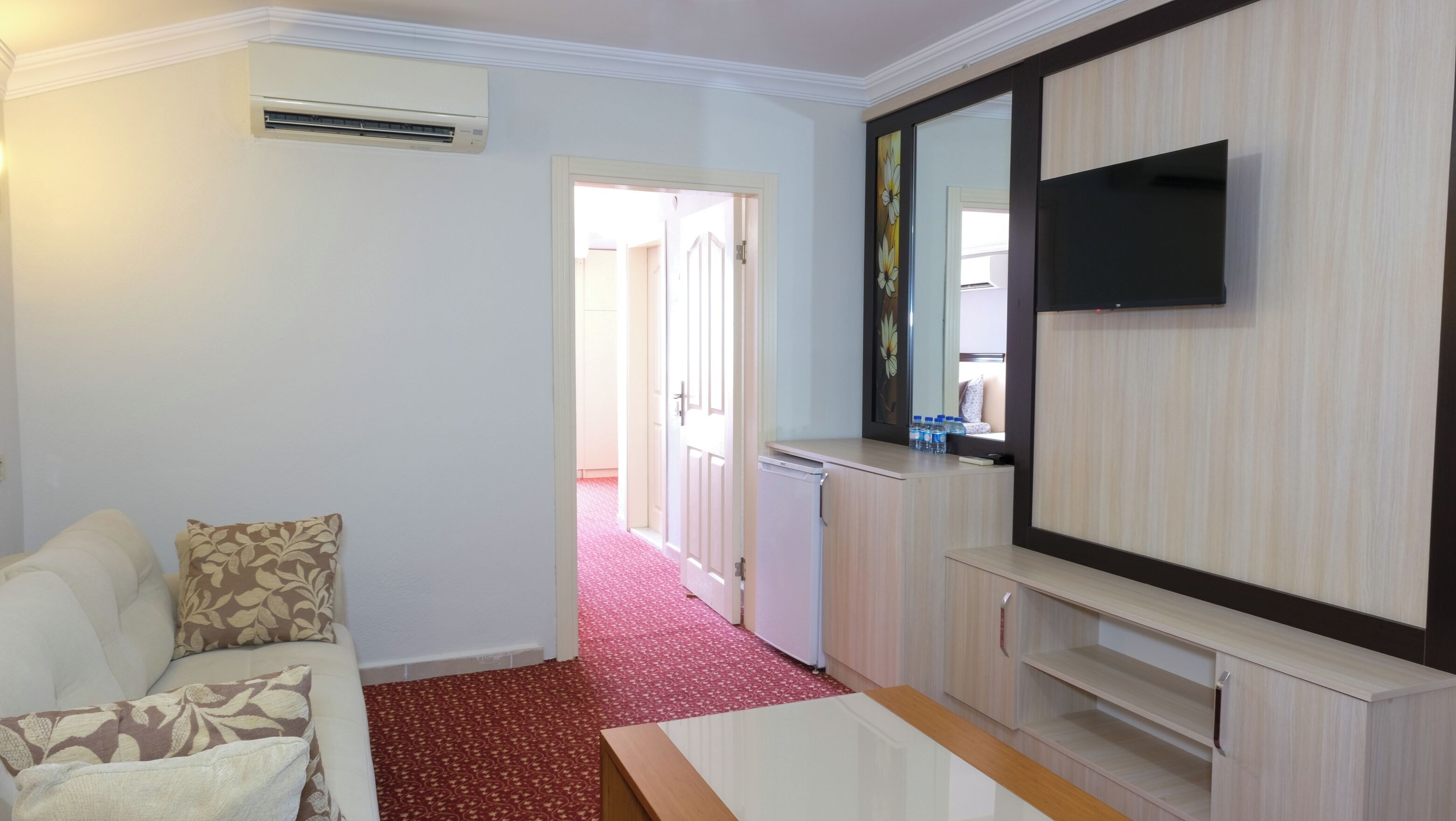 A hotel room with a white sofa, a red carpet, a flat-screen TV, and a minibar.