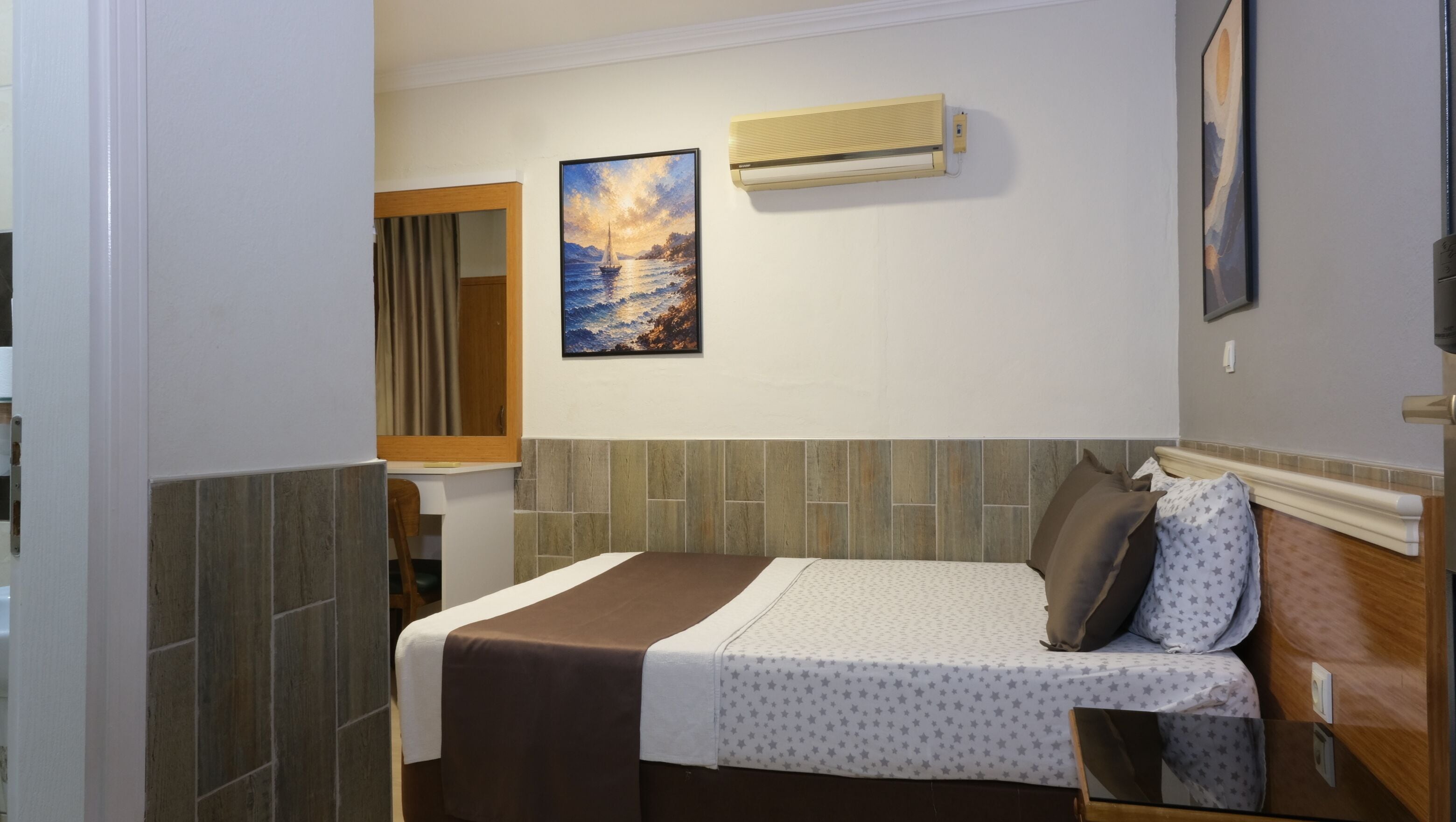 Habitación de hotel con una cama, un cuadro, aire acondicionado y un espejo.