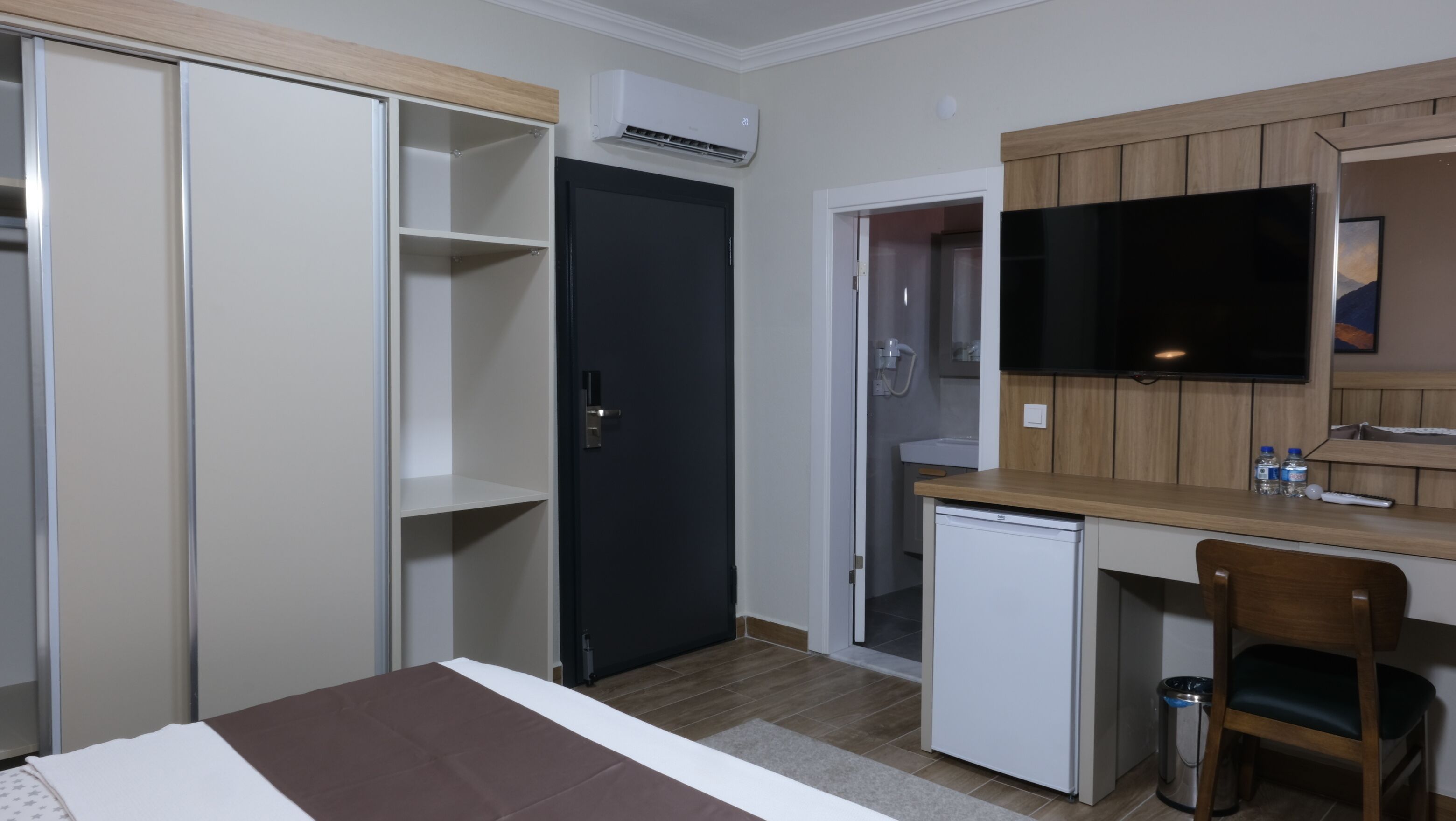 Habitación de hotel pequeña con cama, escritorio, silla, televisión y refrigerador.