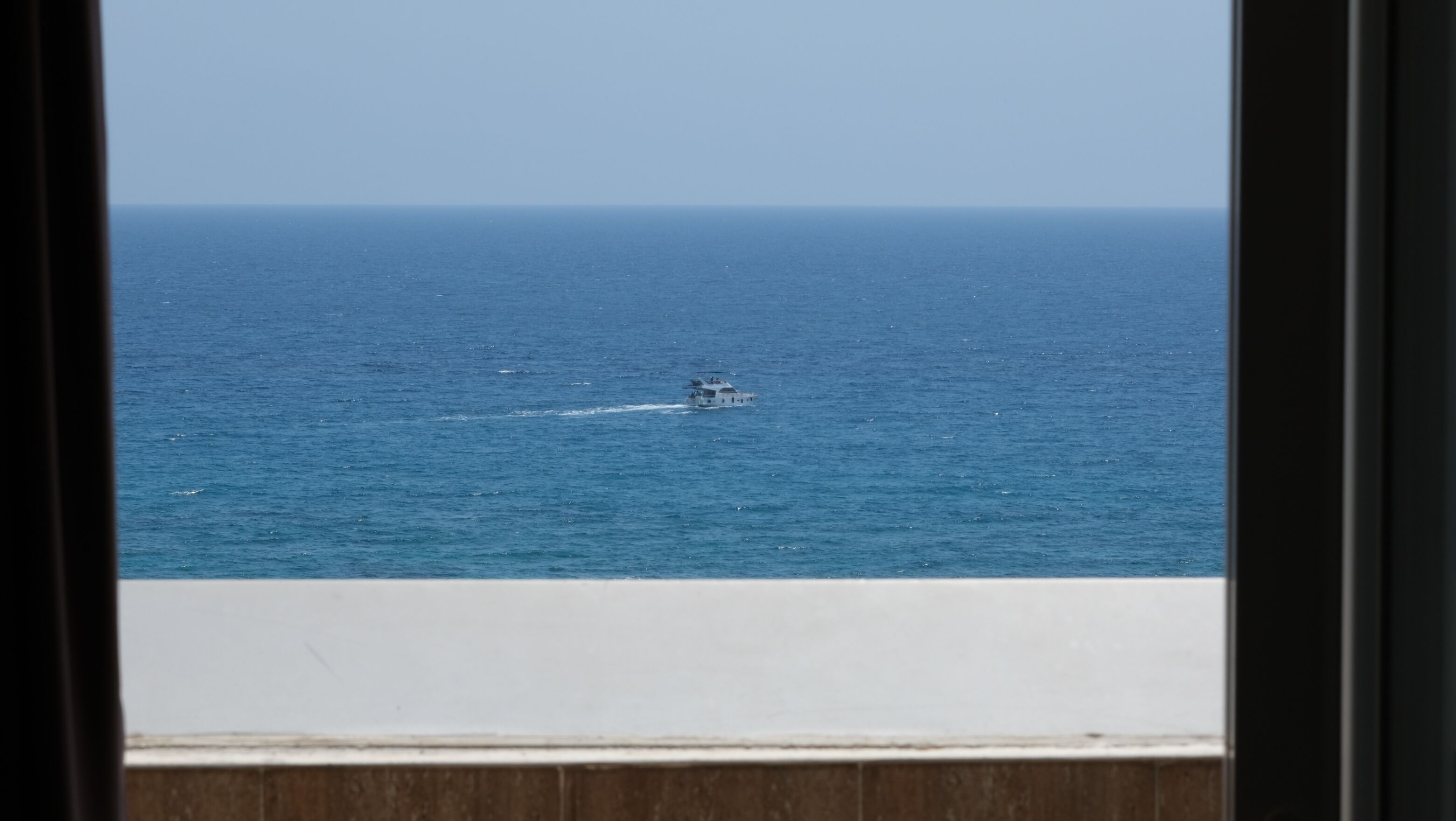 Uitzicht op de oceaan vanuit een raam, met een heldere horizon.