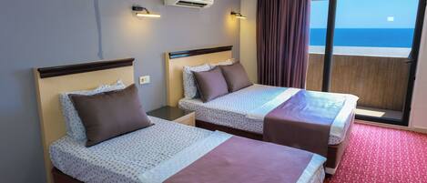 A hotel room with two beds, a balcony with a view of the sea, and an air conditioning unit on the wall.