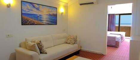 A room with a sofa, a painting, an air conditioner, and a view of the sea.