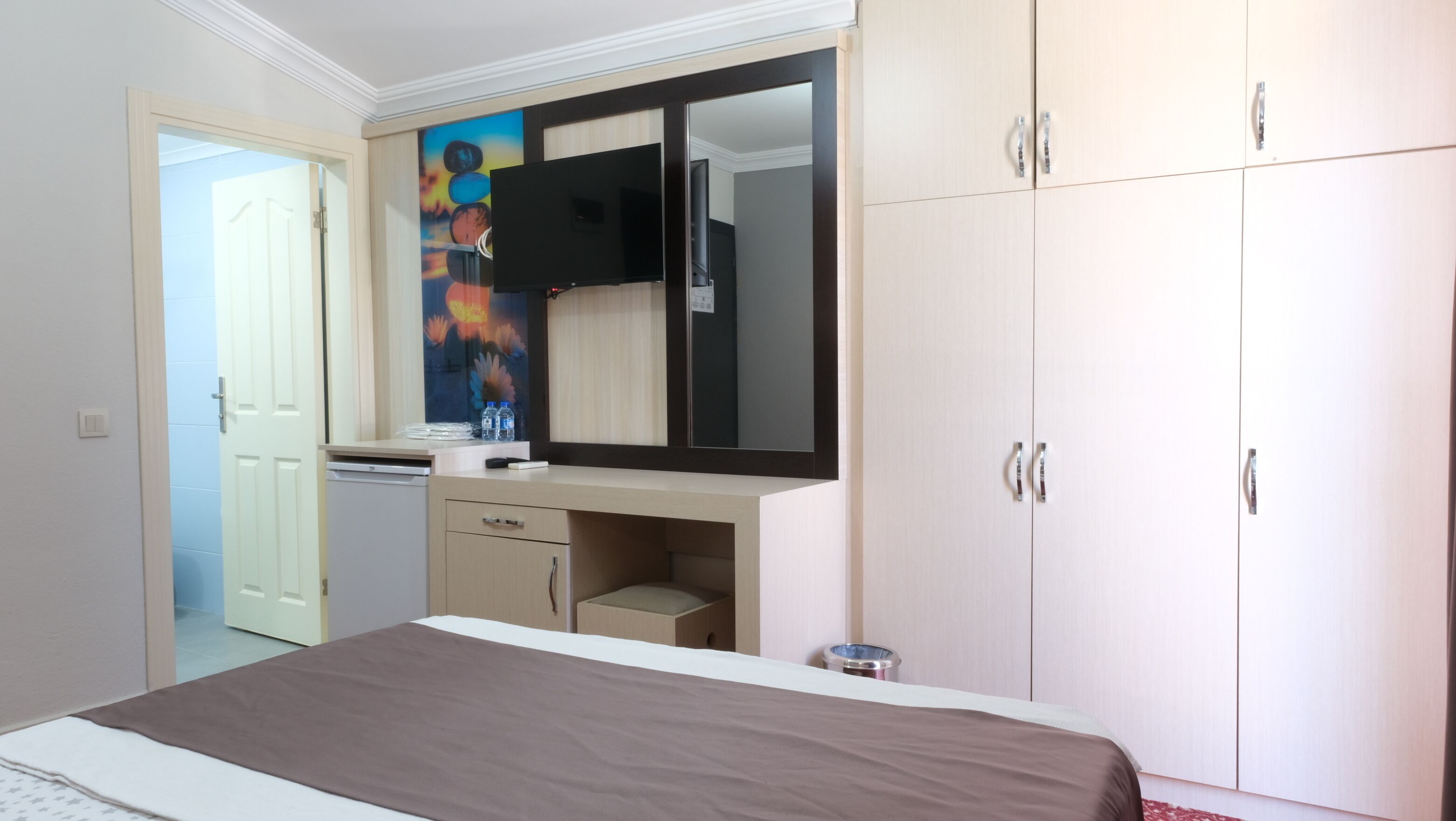 Een hotelkamer met een bed, een bureau met een spiegel, een televisie en een kledingkast.