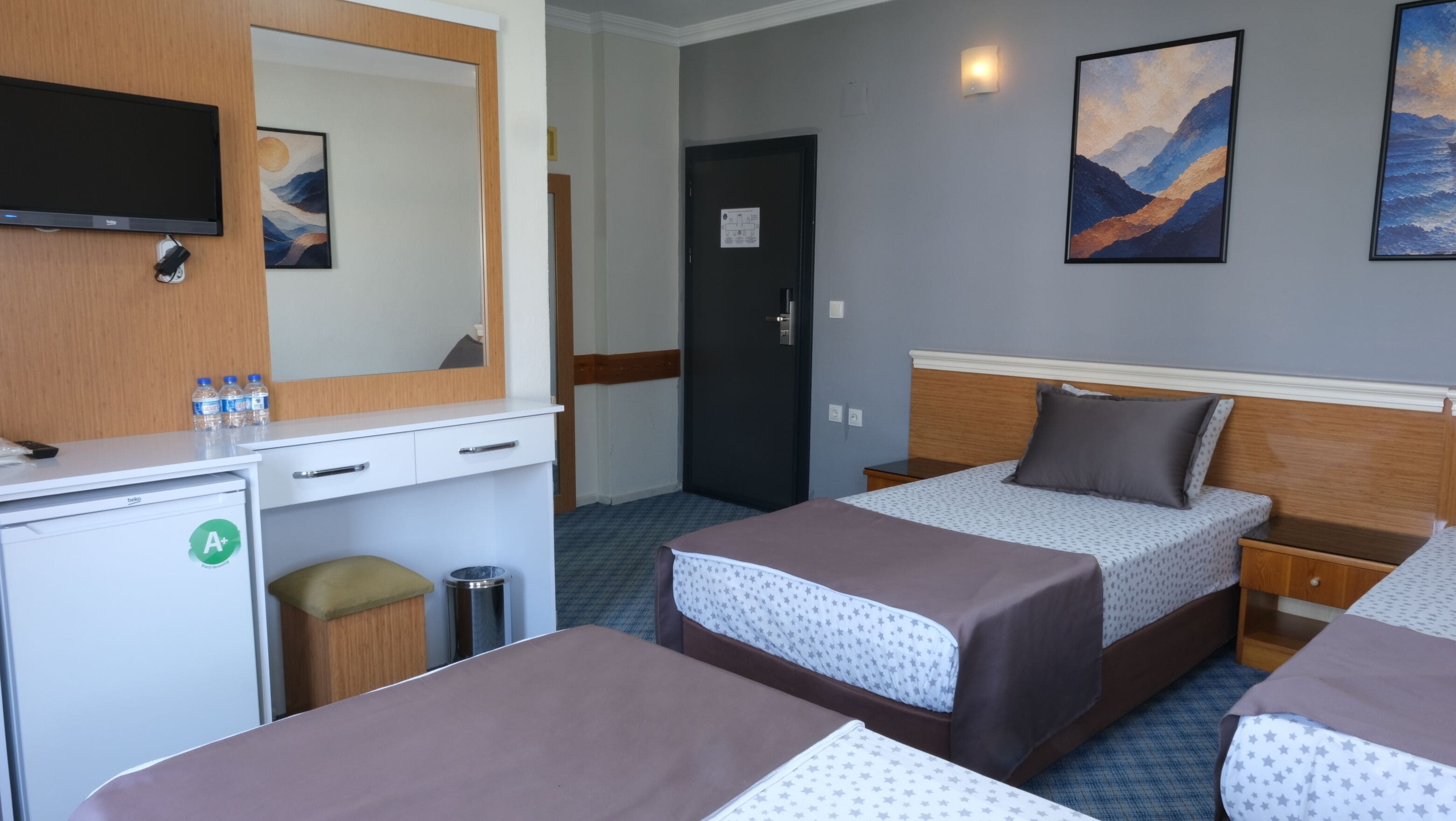 Ett hotellrum med två sängar, ett skrivbord, en spegel och konstverk på väggarna.