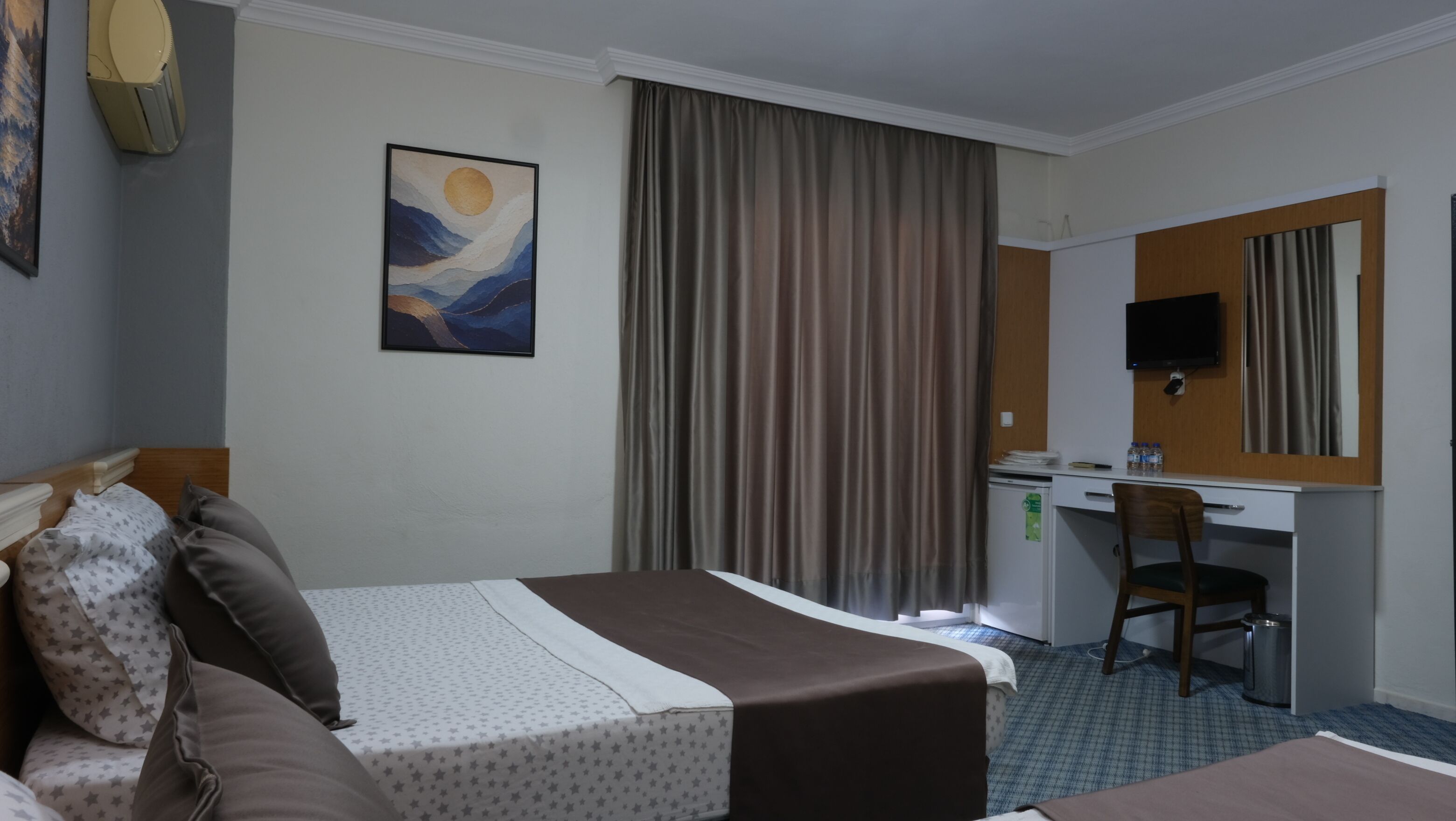 Una camera d'albergo con un letto, una scrivania, una sedia, un televisore e un quadro appeso al muro.