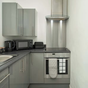 A compact kitchen with a microwave, toaster, kettle, and oven.
