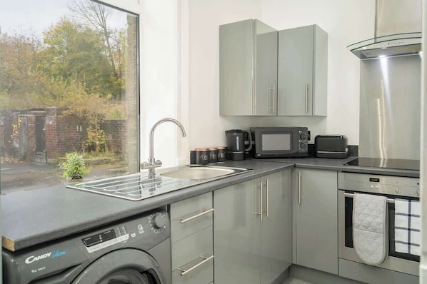 A compact kitchen with a washing machine, a microwave, a toaster, and a sink.