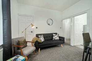 A living room with a black sofa, a round mirror, and a floor lamp.