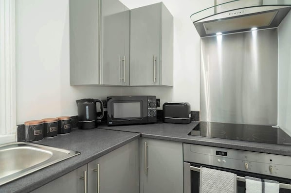 Una cocina moderna con electrodomésticos de acero inoxidable, incluyendo un microondas, tostadora y hervidor, y armarios grises.