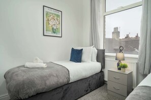 Ein modernes Schlafzimmer mit Bett, Nachttisch, Lampe und Fenster mit Blick auf die Stadt.