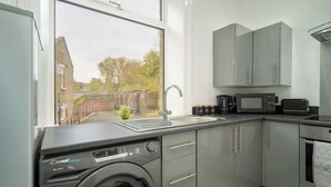 Une cuisine de taille réduite avec des meubles gris, un lave-linge, un four à micro-ondes et un évier.