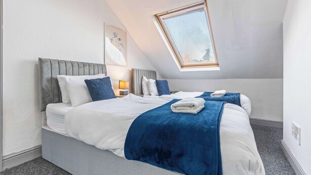 A bedroom with a bed, pillows, a blanket, a bedside table with a lamp, and a skylight. - Lily House - 3 Bed WIFI & Parking Hull (Kingston upon Hull)