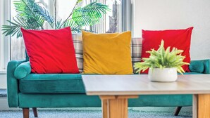 A teal sofa with three cushions in red, yellow, and plaid, a small white table, and a potted plant. - Lily House - 3 Bed WIFI & Parking Hull (Kingston upon Hull)