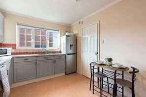 Une cuisine compacte avec des meubles gris, un réfrigérateur en acier inoxydable, un four à micro-ondes et une petite table à manger avec des chaises.