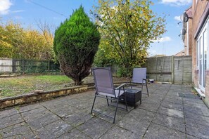Un espace patio avec deux chaises et une petite table, entouré d’un mur de briques et d’une clôture en bois.