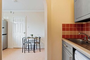 Une cuisine de taille réduite avec une porte blanche, une petite table à manger avec deux chaises et un pare-feu rouge en carreaux.