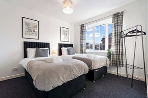 Une chambre d’hôtel avec deux lits, une fenêtre avec des rideaux, un porte-vêtements et des œuvres d’art accrochées aux murs.