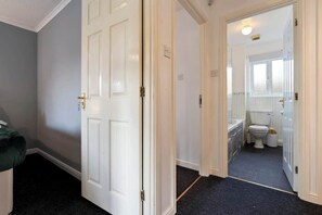 Un couloir menant à une salle de bain équipée de toilettes, d’un lavabo et d’une fenêtre.