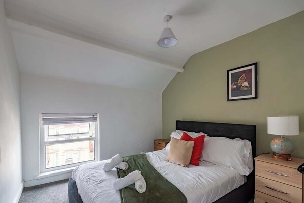 A bedroom with a bed, a window, a nightstand, a lamp, and a framed picture on the wall.