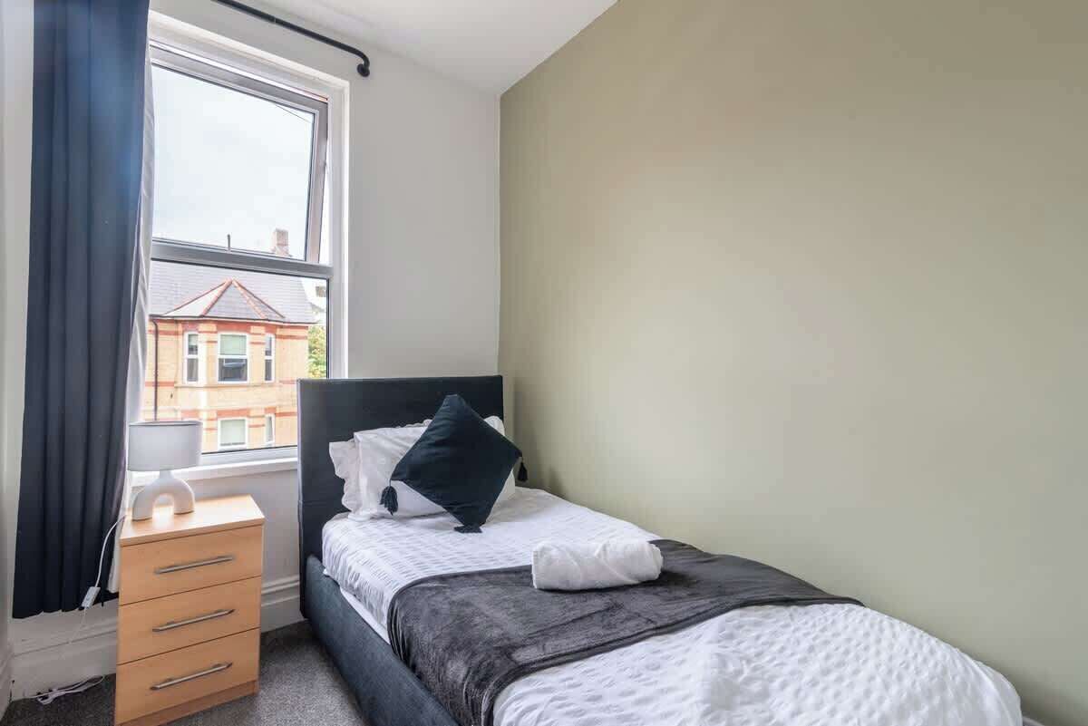 A bedroom with a bed, a bedside table, a lamp, and a window with curtains.