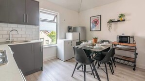 A compact kitchen with grey cabinets, a dining table with chairs, a microwave, and a small refrigerator.