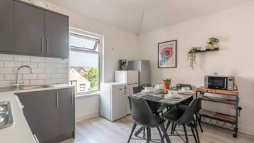 A compact kitchen with grey cabinets, a dining table with chairs, a microwave, and a small refrigerator.