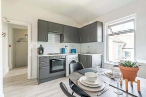 Et moderne køkken med lysegrå skabe, en indbygget ovn og et spiseområde med et bord dækket til to personer.