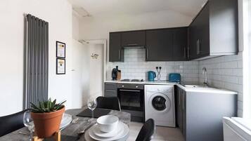 A compact kitchen with dark cabinets, a washing machine, and a small dining area with a table and chairs.