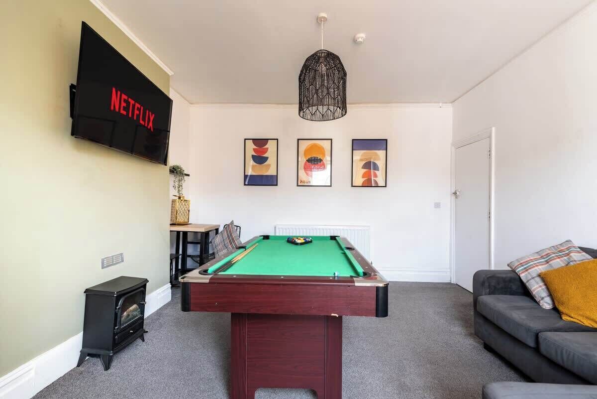 Una sala de estar con mesa de billar, un sofá, televisor montado en la pared y chimenea.