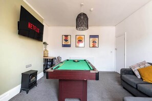 Ein Wohnzimmer mit Billardtisch, einer Couch, einem an der Wand befestigten Fernseher und einem Kamin.