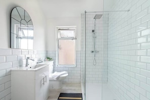 A modern bathroom with white tiles, a sink, a toilet, and a shower.