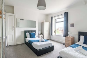 A modern bedroom with a large bed, a bedside table, a wardrobe, and a window with curtains.