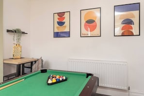 Ein Billardtisch mit Kugeln, ein Tisch mit einer Vase und drei gerahmte Kunstwerke an der Wand.