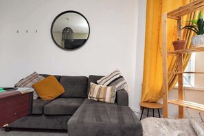 A modern living room with a grey sectional sofa, a round mirror on the wall, and a wooden shelf with plants.