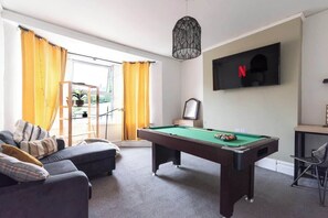 A room with a pool table, a sofa, a TV, and a window with curtains.