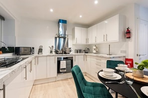 Una cocina moderna con armarios blancos, electrodomésticos de acero inoxidable y una silla tapizada en color aguamarina.