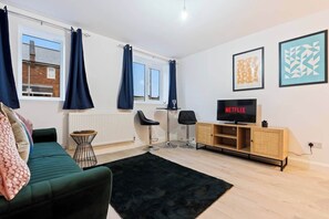 Ein modernes Wohnzimmer mit einem grünen Sofa, einem schwarzen Teppich, einem Holz-TV-Schrank und einem großen Fenster mit Vorhängen.
