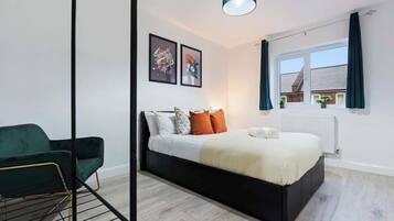 Ein modernes Schlafzimmer mit einem Bett, einem grünen Sessel und Kunstwerken an der Wand.