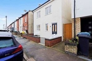 A residential street with terraced houses, a parked car, and a visible trash bin. - Ruby’s Retreat-4 Bed- Contractor Disc- WiFi (Hertfordshire)