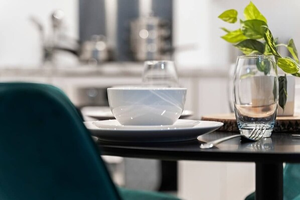 A dining table with a white bowl, a glass of water, and a fork. There is a green plant in a vase to the right.