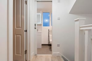 Un pasillo estrecho con una puerta a la izquierda y una ventana que da a un baño a la derecha.