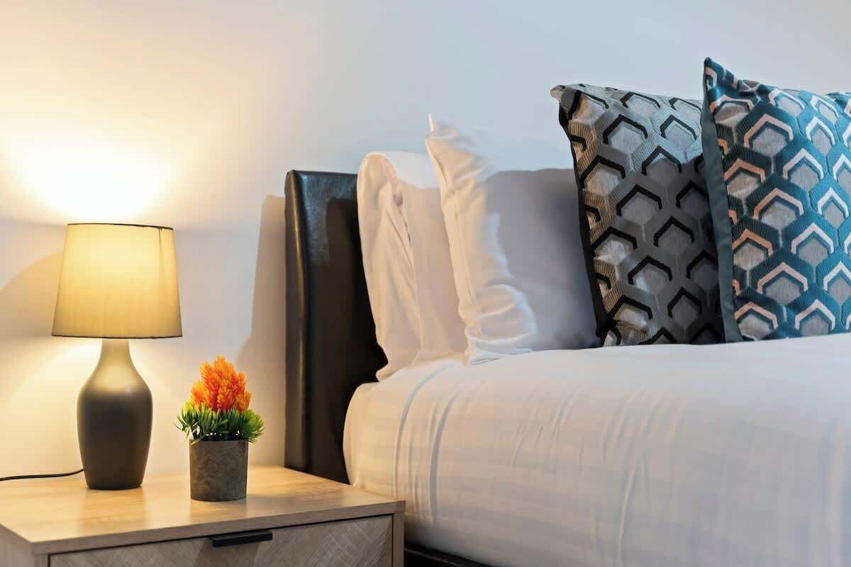 A neatly made bed with patterned pillows, a bedside lamp, and a small potted plant on a wooden nightstand.