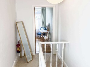 Ein Flur mit weißer Geländer, einem Feuerlöscher und einem an der Wand lehnten Spiegel.