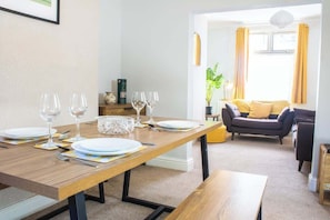 A dining area with a wooden table set for four, a sofa, and a plant in the background.