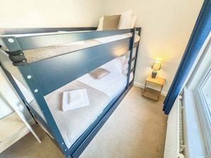 A bunk bed with a headboard, a bedside table with a lamp, and a window with curtains.