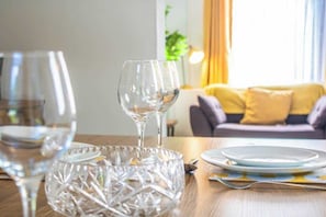 Ein Esstisch mit klarem Glasgeschirr und Tellern, eine dekorative Glasvase und eine Couch im Hintergrund.