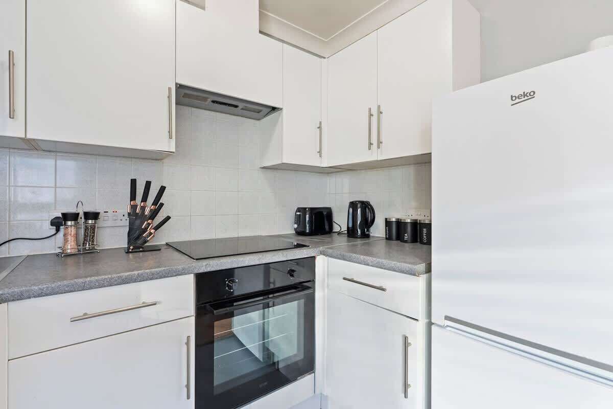 A modern kitchen with white cabinets, a black oven, and a white refrigerator.